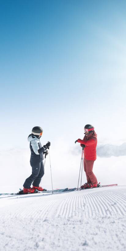 Zwei Skifahrer stehen auf frisch präparierter Piste in Ski amadé mit Blick über wolkenverhangenes Tal