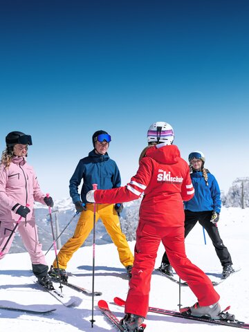 Skilehrerin zeigt vier Skischülern in bunter Kleidung Übungen auf sonniger, verschneiter Piste in Ski amadé