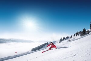 Skier in red suit carves turn on groomed slope with view into the valley in Ski amadé