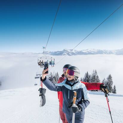 Zwei Skifahrer machen ein Selfie auf sonniger Piste mit Sessellift und Alpenblick in Ski amadé