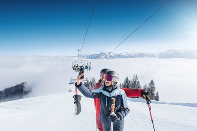 Two skiers take a selfie on sunny slope with chairlift and mountain view in Ski amadé