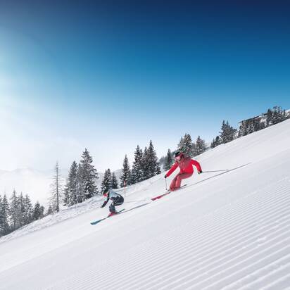 Two skiers ski in parallel on freshly groomed slope with powder snow and sunlight in Ski amadé