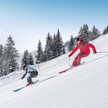 Two skiers ski in parallel on freshly groomed slope with powder snow and sunlight in Ski amadé