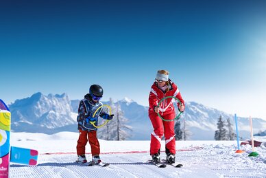Ski instructor and child practise with coloured rings on sunny slope in the snow at Best Learn2Ski amadé course