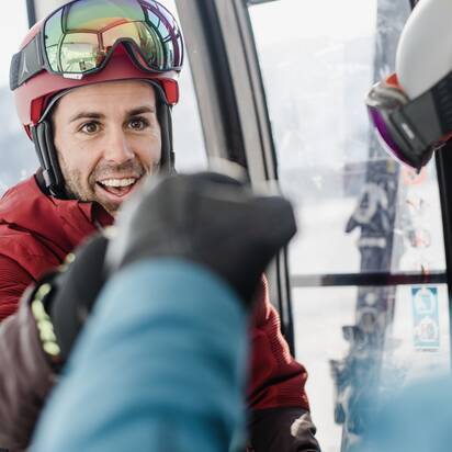 Ein Skifahrer in rotem Skianzug gibt einem Freund in der Gondel einen Fistbump. | © Ski amadé