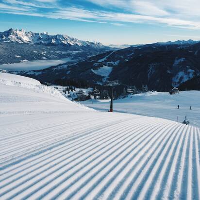 Frisch präparierte Skipiste mit Sessellift und verschneiten Bergen. | © Ski amadé