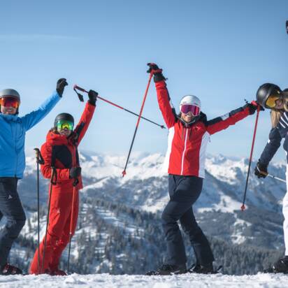Vier Freunde in Skiausrüstung stehen auf der Piste und Strecken die Arme freudvoll in die Höhe. | © Ski amadé