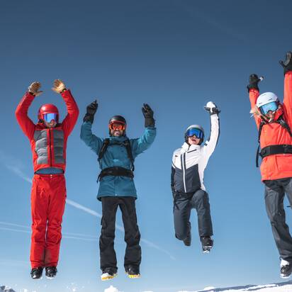 Vier Skifahrer springen gleichzeitig in die Luft vor blauem Himmel und verschneiten Bergen | © Ski amadé