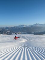 Two people ski down a freshly groomed slope and swirl up the snow