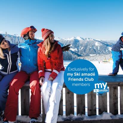 Four skiers in colorful ski outfits sit relaxed on a wooden bench, enjoying the sun with a beautiful mountain view.