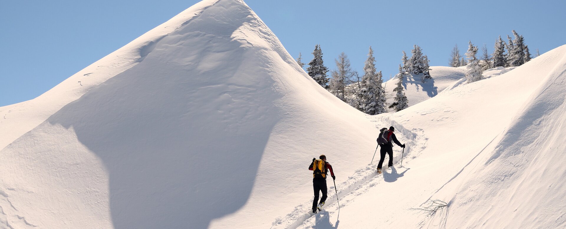 Zwei Skitourengeher gehen zwischen zwei mit Viel Schnee bedeckten Hügeln hindurch den Berg hinauf | © Peter Rohrmoser